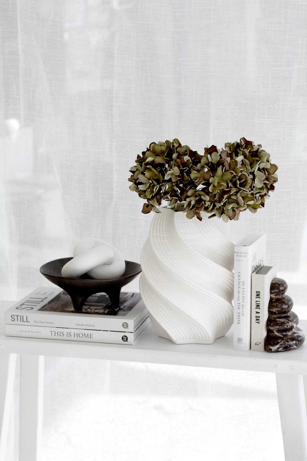 White 3D printed vase of dried hydrangea on a slim console lit by a sheer curtained window
