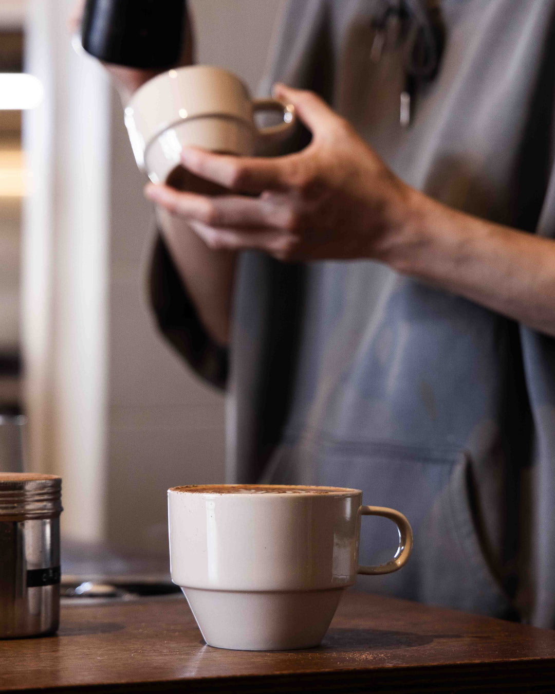 Barista holding Hudson Mugs, with a finished coffee on the counter