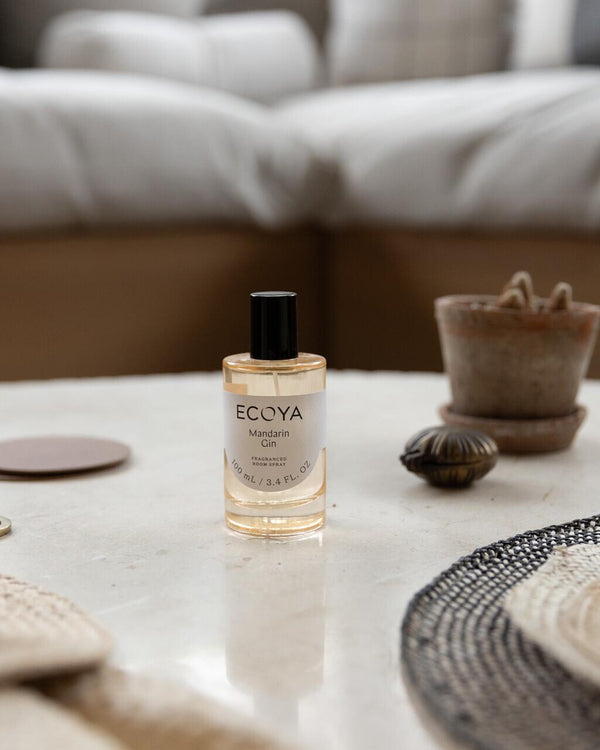 ECOYA Mandarin Gin fragranced room spray in a clear glass bottle with black cap, styled on a marble coffee table with natural decor accents.