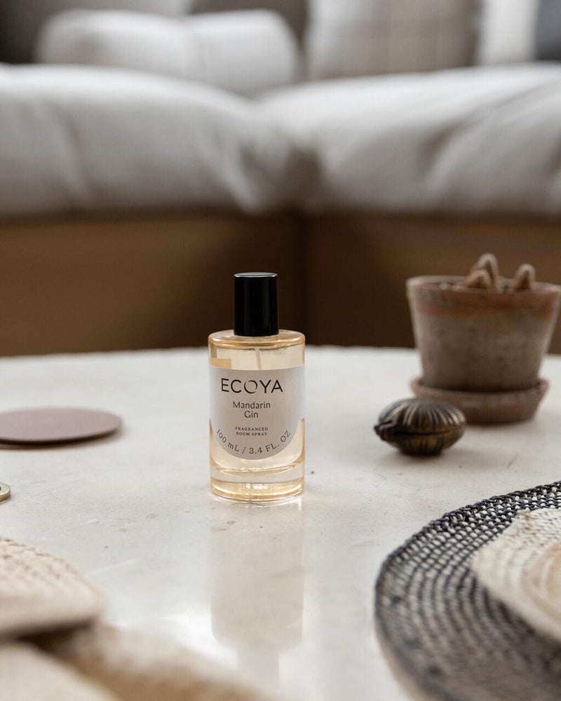 ECOYA Mandarin Gin fragranced room spray in a clear glass bottle with black cap, styled on a marble coffee table with natural decor accents.