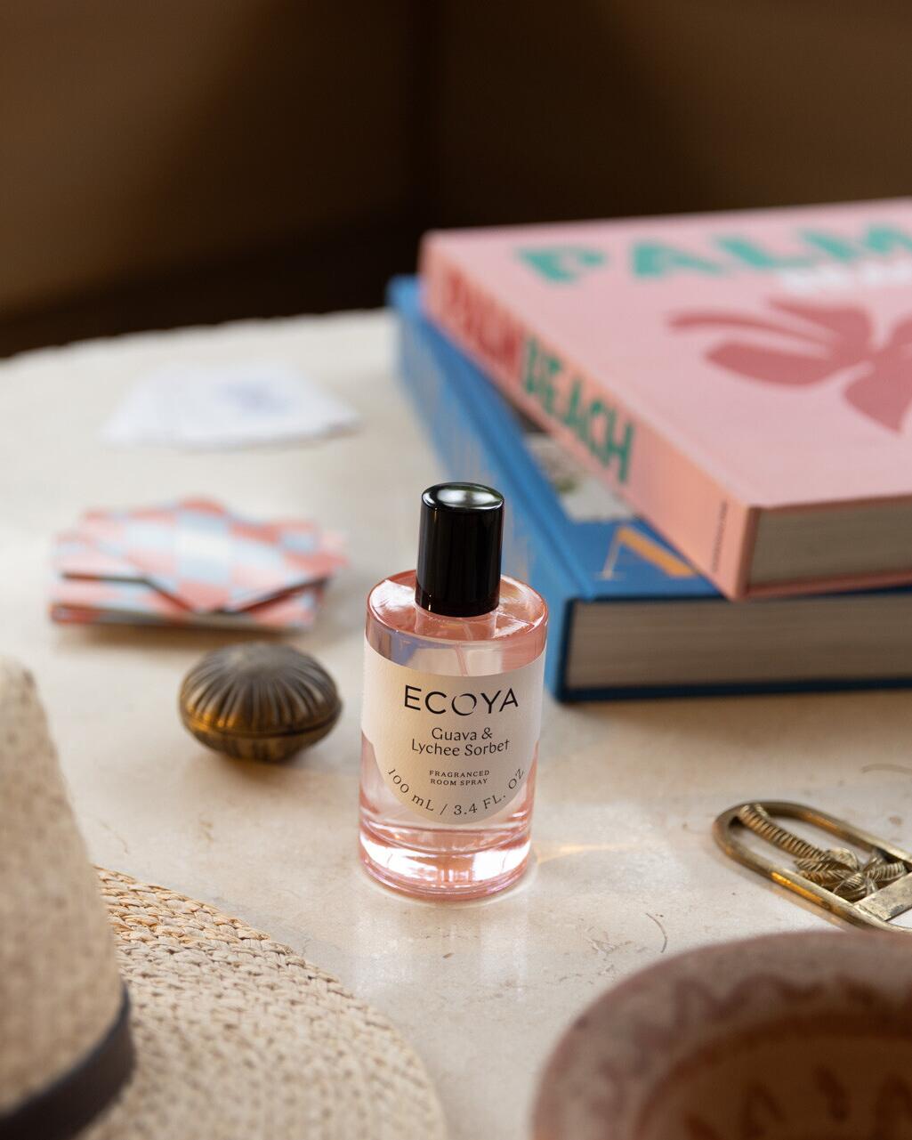 Pink Ecoya room spray on a stone table with a shell, brass keyring and a pink book