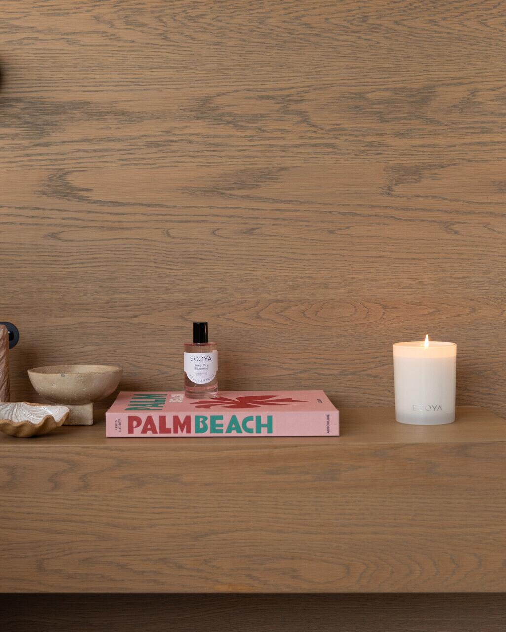 Ecoya room spray, candle and books on a warm timber shelf