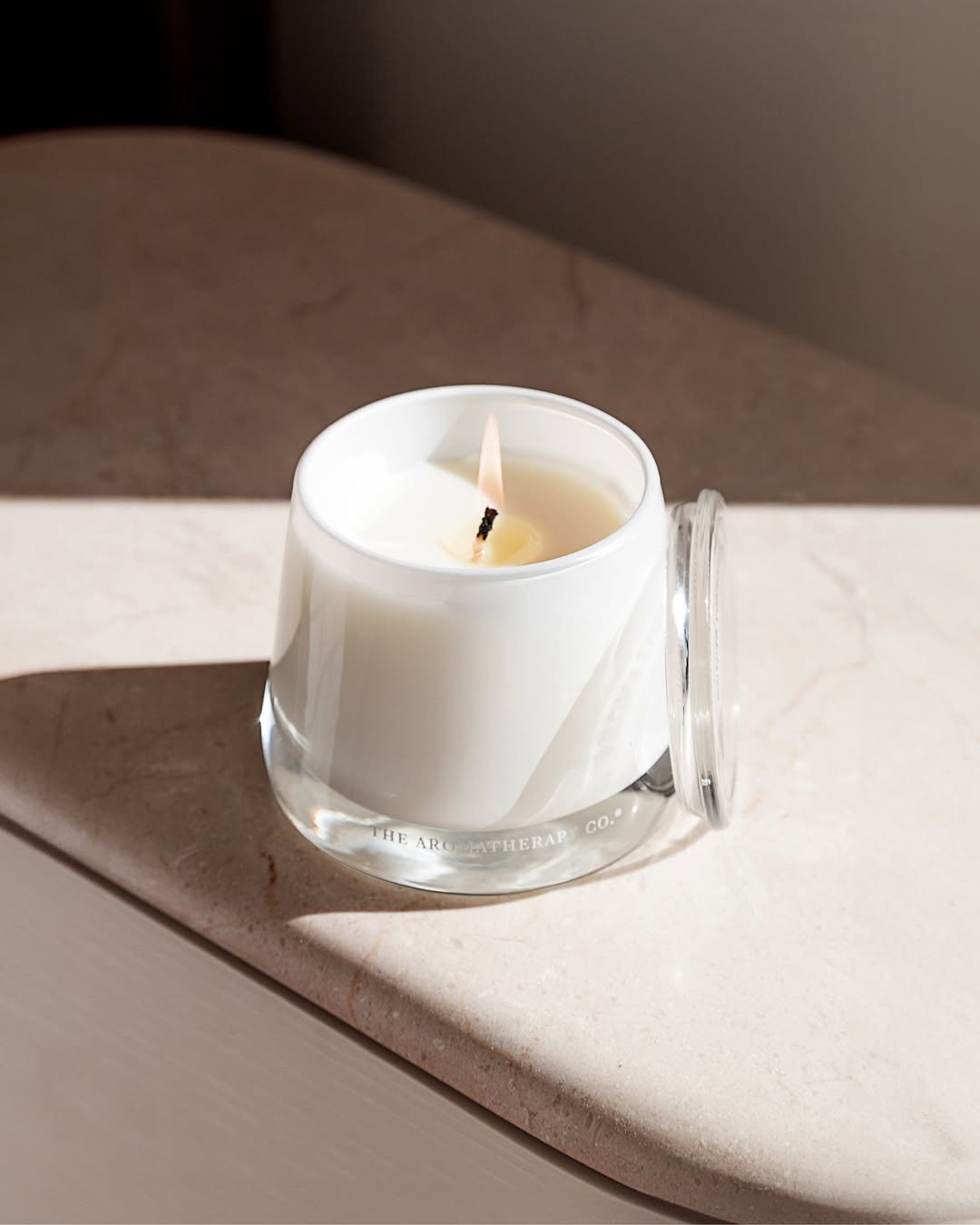Lit Embrace candle with its glass lid on a pale stone ledge in warm afternoon light