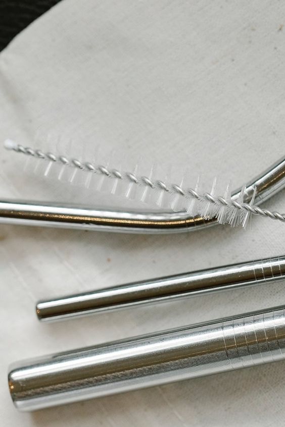 Wire straw brush laid across a bent stainless steel straw on linen, two more steel straws below