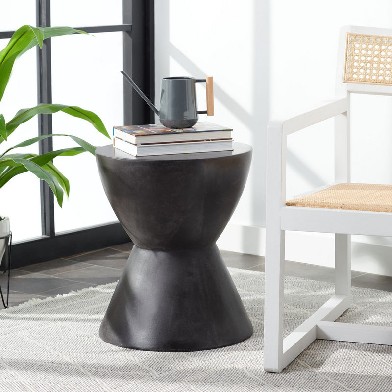 A Flux Home Westside Round Accent Table - Stonewash / Black next to a chair and a potted plant.
