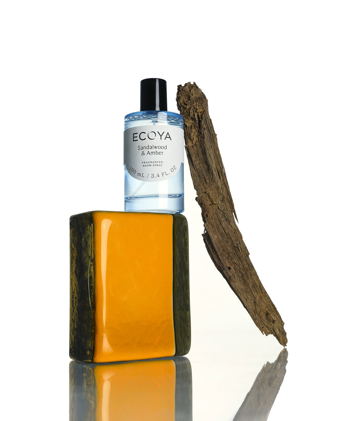Ecoya room spray in pale blue glass on an amber block beside a piece of driftwood