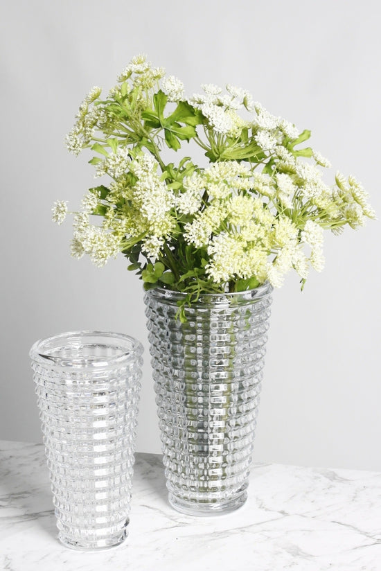 Cut glass vase of white blossom beside a smaller faceted tumbler on marble