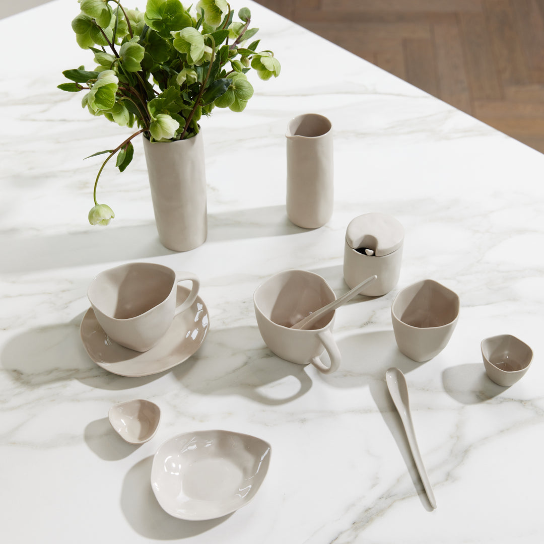 Haan stoneware dishes, cups and vases in bone on a marble table with green flowers