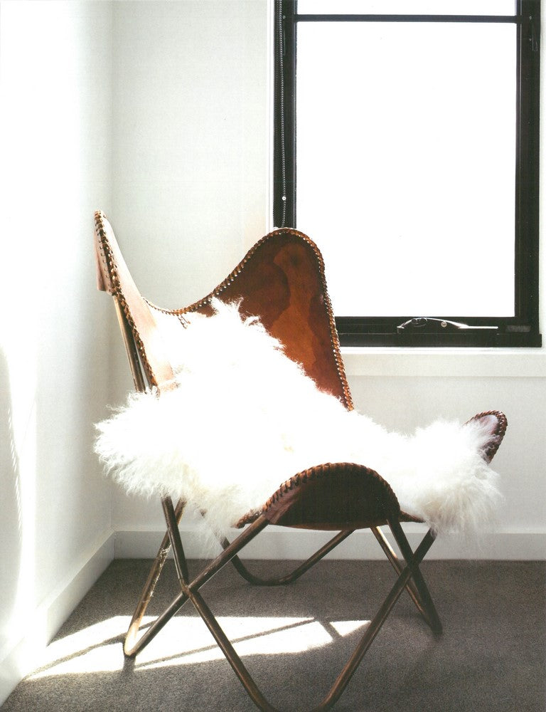 Scandi spread showing a tan leather butterfly chair draped with a white sheepskin beside a window