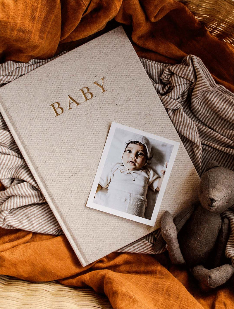 Oatmeal linen Write To Me Baby journal on rust fabric with a baby photo and a knitted toy