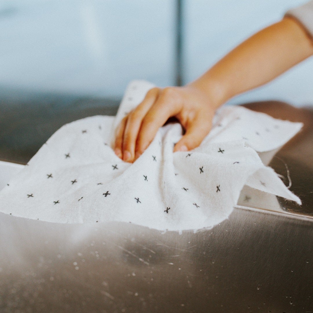 A person using a Good Change reusable bamboo towel to clean a cloth in a sink.
