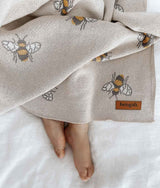 A baby is laying on a bed with a Honeybee Blanket from Bengali Collections.