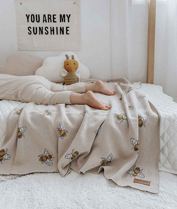 A child laying on a bed with a Bengali Collections Honeybee Blanket that says you are my sunshine.