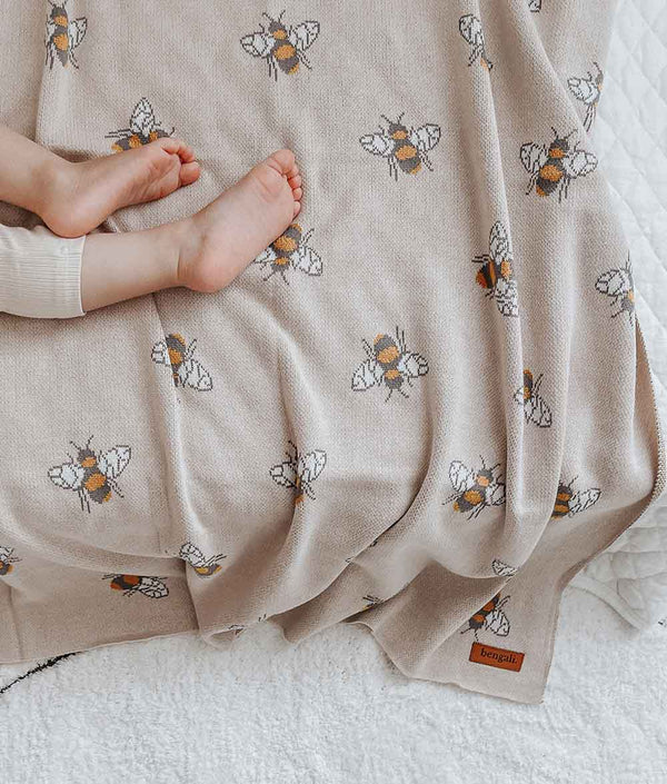 A baby laying on a Honeybee Blanket with bees on it, from Bengali Collections.