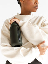 A woman holding a black Day Bottle with Hydration Tracker from Bink, emphasizing hydration tracking.