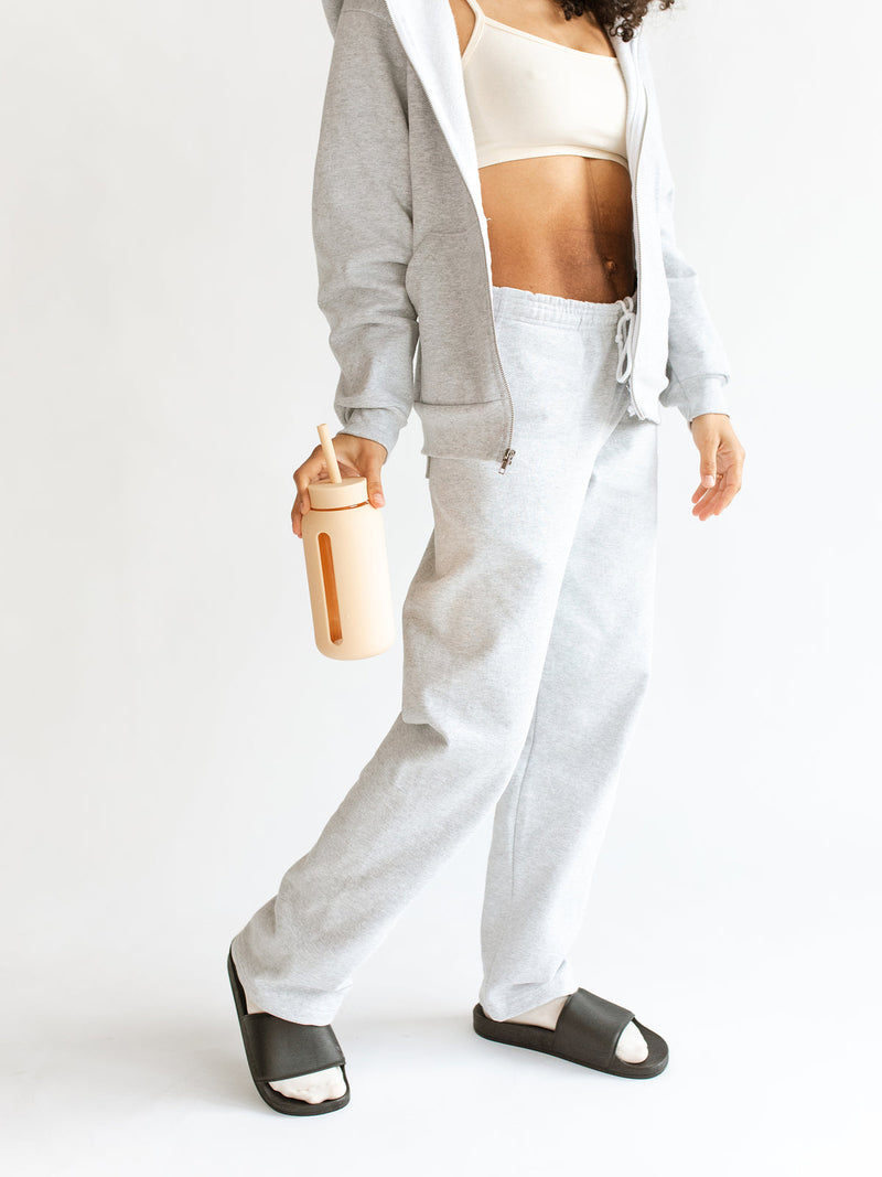 A woman in grey sweatpants and a hoodie holding a Bink Day Bottle with Hydration Tracker for hydration tracking.