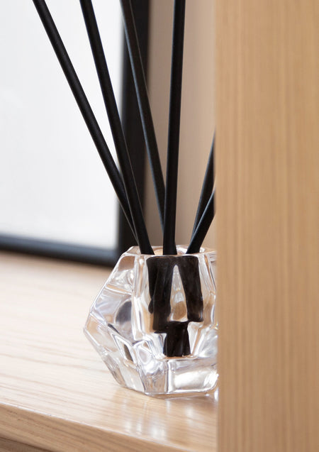 Close view of black aroma sticks in a faceted glass holder on a timber surface