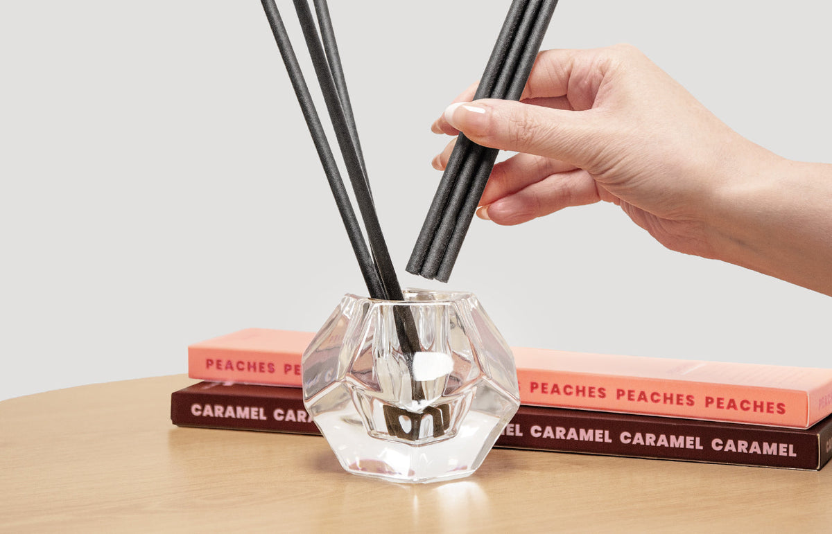 Hand placing black aroma sticks into a faceted glass holder on stacked fragrance boxes