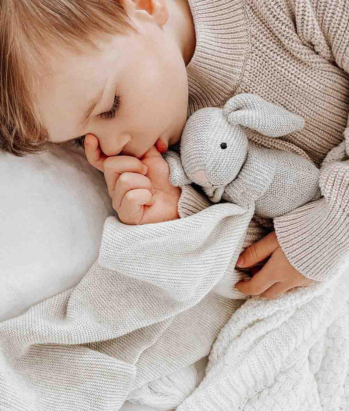 A young boy sleeping with a BUNNY SNUGGLY - NATURAL MARLE from Bengali Collections.