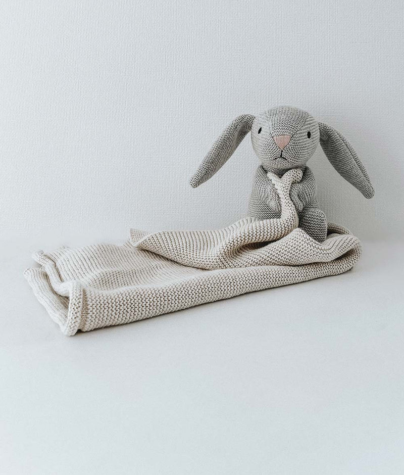 A BUNNY SNUGGLY - NATURAL MARLE from Bengali Collections lying on a white blanket.