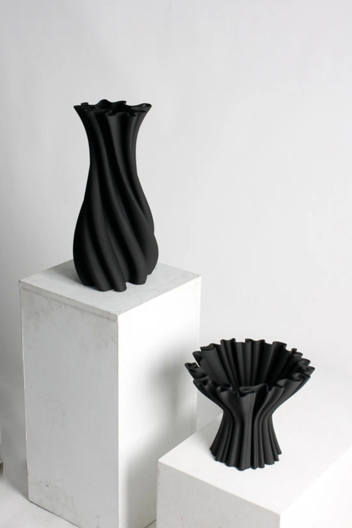 Black Cleo compote vase on a white plinth beside a taller twisted black vase