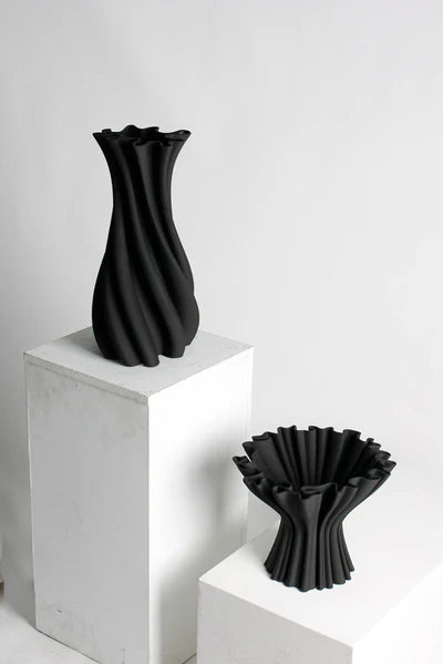 Black Cleo compote vase on a white plinth beside a taller twisted black vase