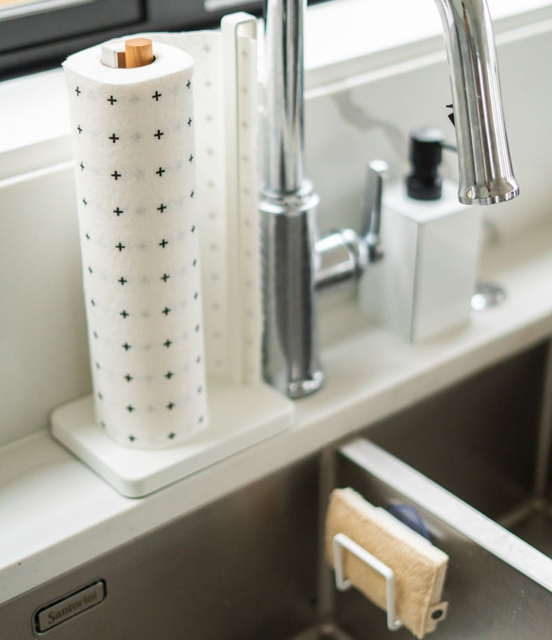 A kitchen sink with a paper towel holder perfect for eco-friendly cleaning with Good Change Eco Scrubs 2-Pack.
