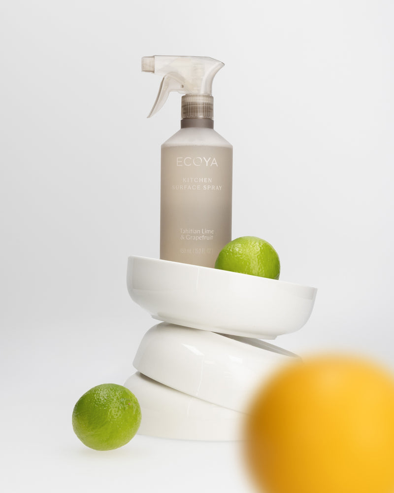 Ecoya Tahitian Lime & Grapefruit kitchen surface spray resting on stacked white bowls with a lime and a lemon