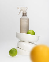 Ecoya Tahitian Lime & Grapefruit kitchen surface spray resting on stacked white bowls with a lime and a lemon