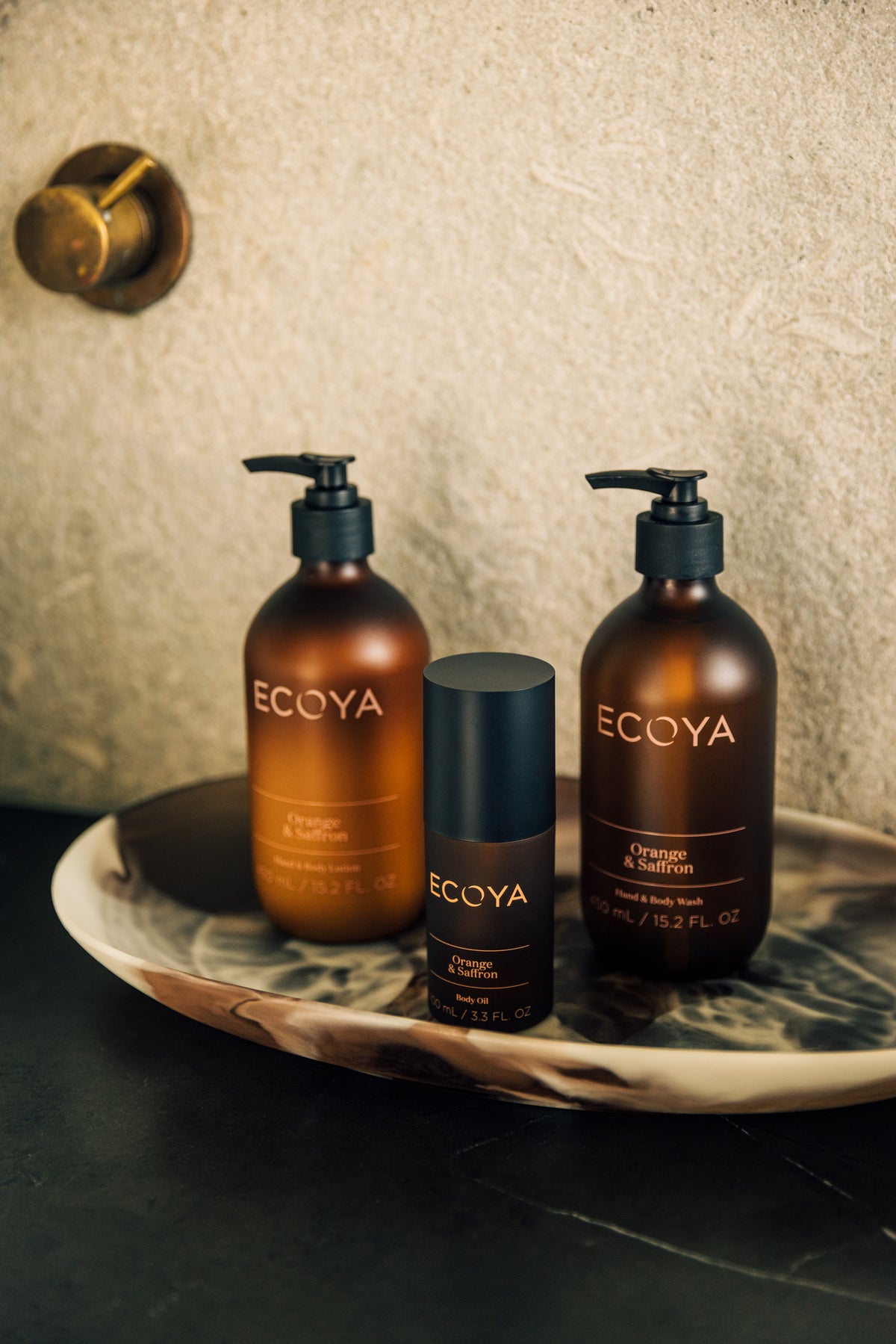 Ecoya Sandalwood & Amber shampoo and conditioner on a dark stone dish against a textured wall