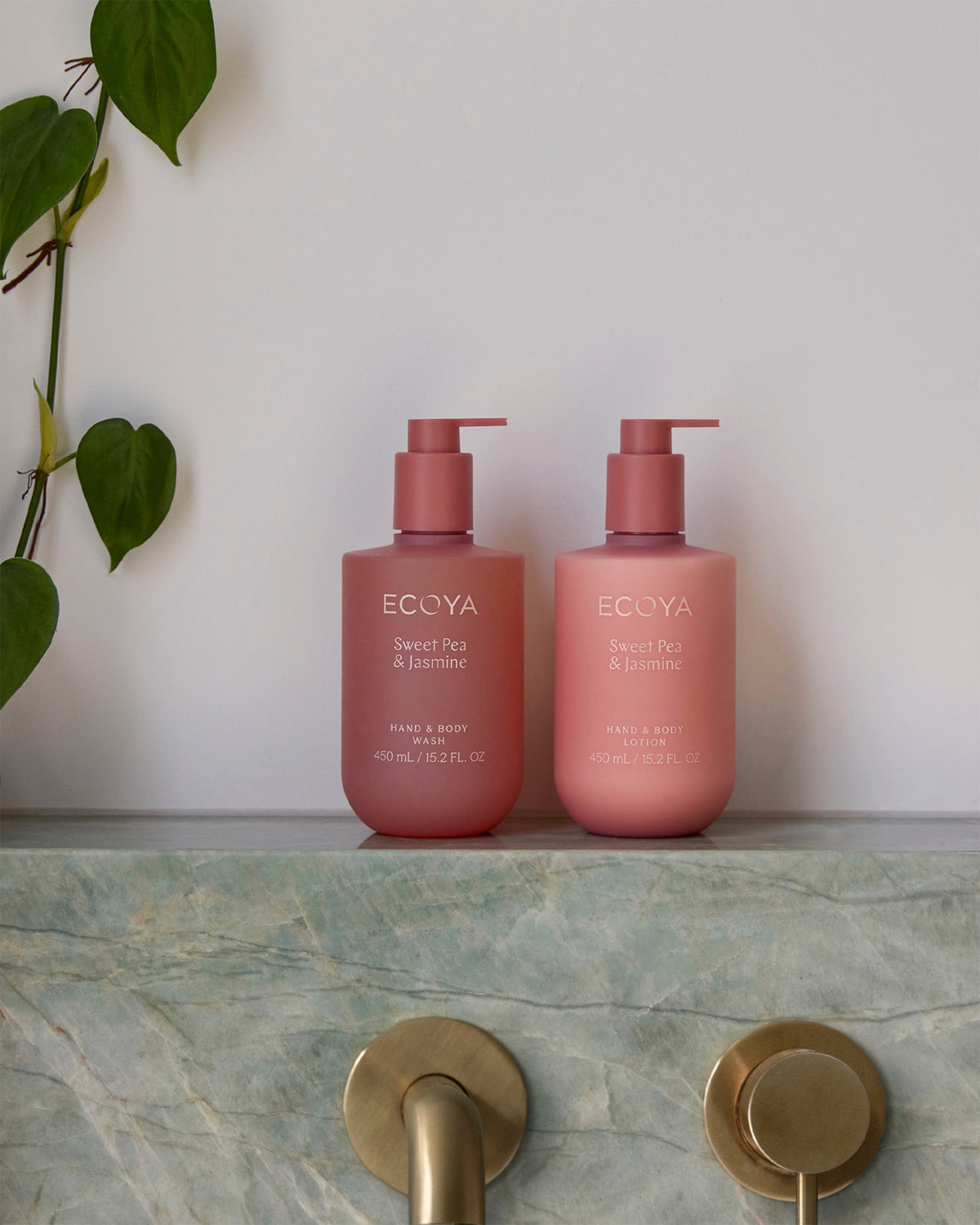 Two rose pink Ecoya lotion bottles on a green marble bench with brass tapware