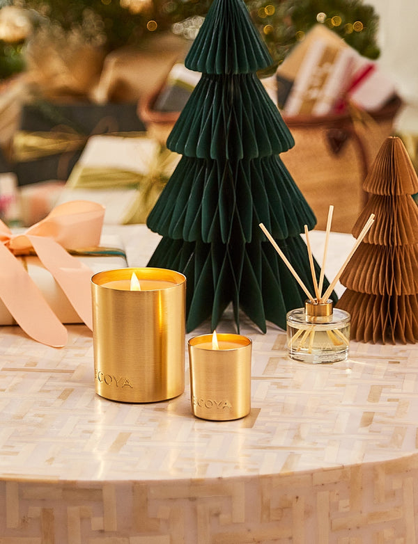 An Ecoya: Holiday Fresh Pine Mini Goldie Candle sits on a table next to a festive season.