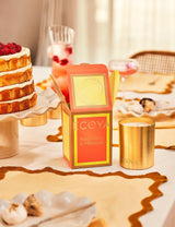 A luxurious table setting featuring an Ecoya Holiday: Raspberry & Hibiscus Goldie Candle and a beautifully wrapped box.