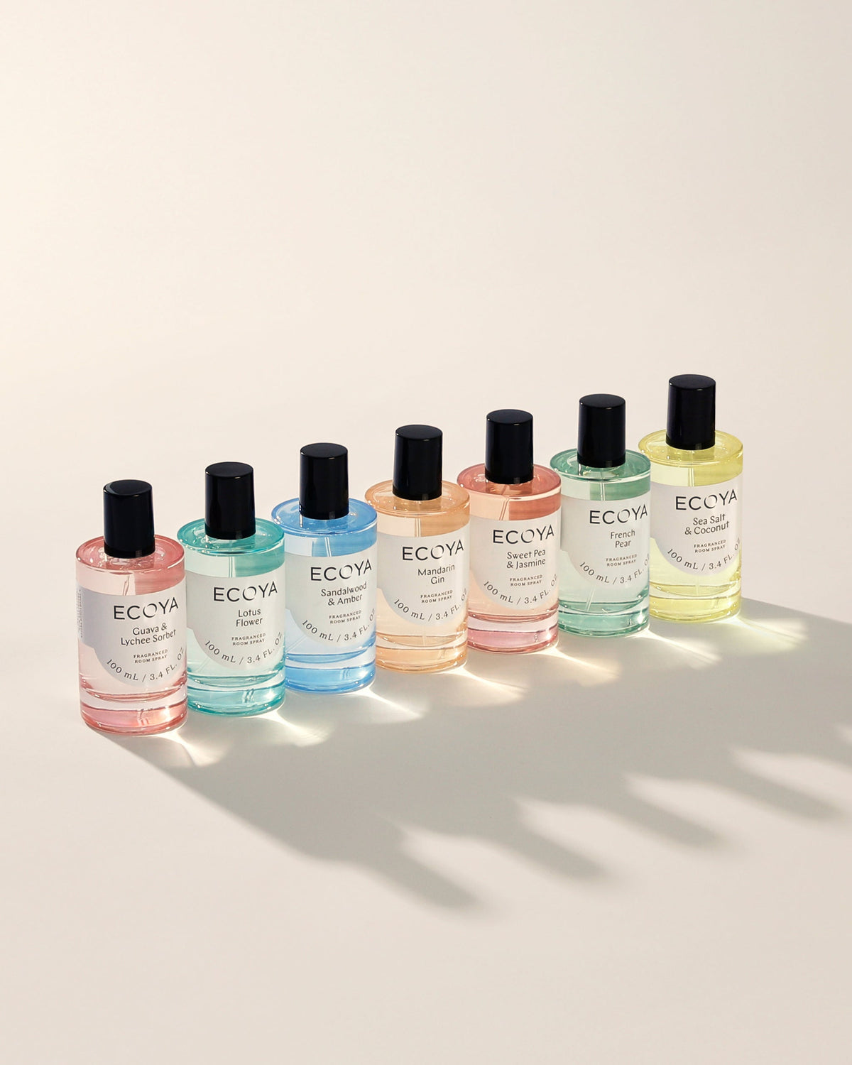 Line of eight Ecoya room sprays in coloured glass bottles casting shadows on cream