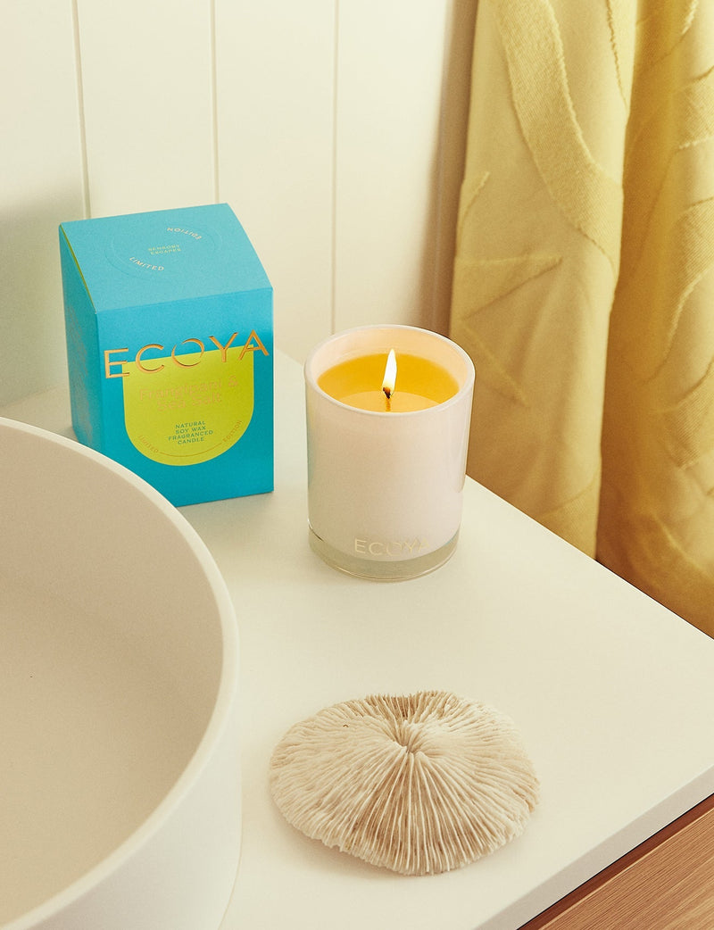 An Ecoya Frangipani & Sea Salt Madison Candle, a perfect gift for home fragrance and design enthusiasts, placed next to a sink in a bathroom.