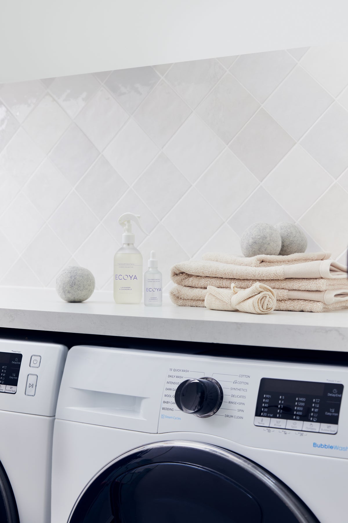 Ecoya laundry liquid with wool dryer balls and a tied bundle of folded towels on a white bench