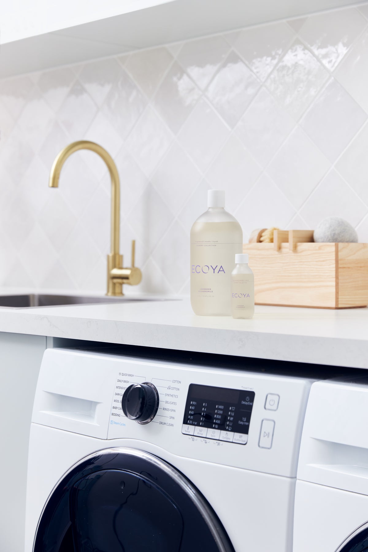 Brass gooseneck tap and sink with Ecoya laundry liquid and a wooden peg box above a washing machine