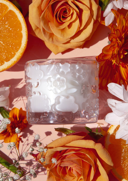 The Fleur D'Oranger candle with roses, orange slices and daisies on a warm peach backdrop