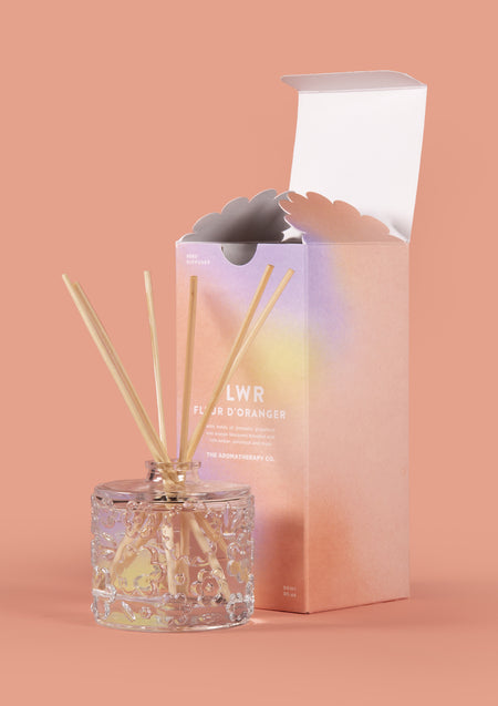 The Fleur D'Oranger diffuser beside its open pastel carton on a warm peach backdrop