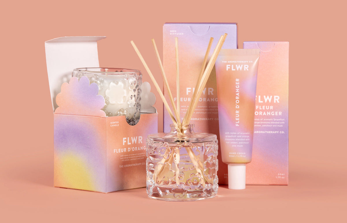 The full Fleur D'Oranger set, candle, diffuser and hand cream with their cartons, on peach