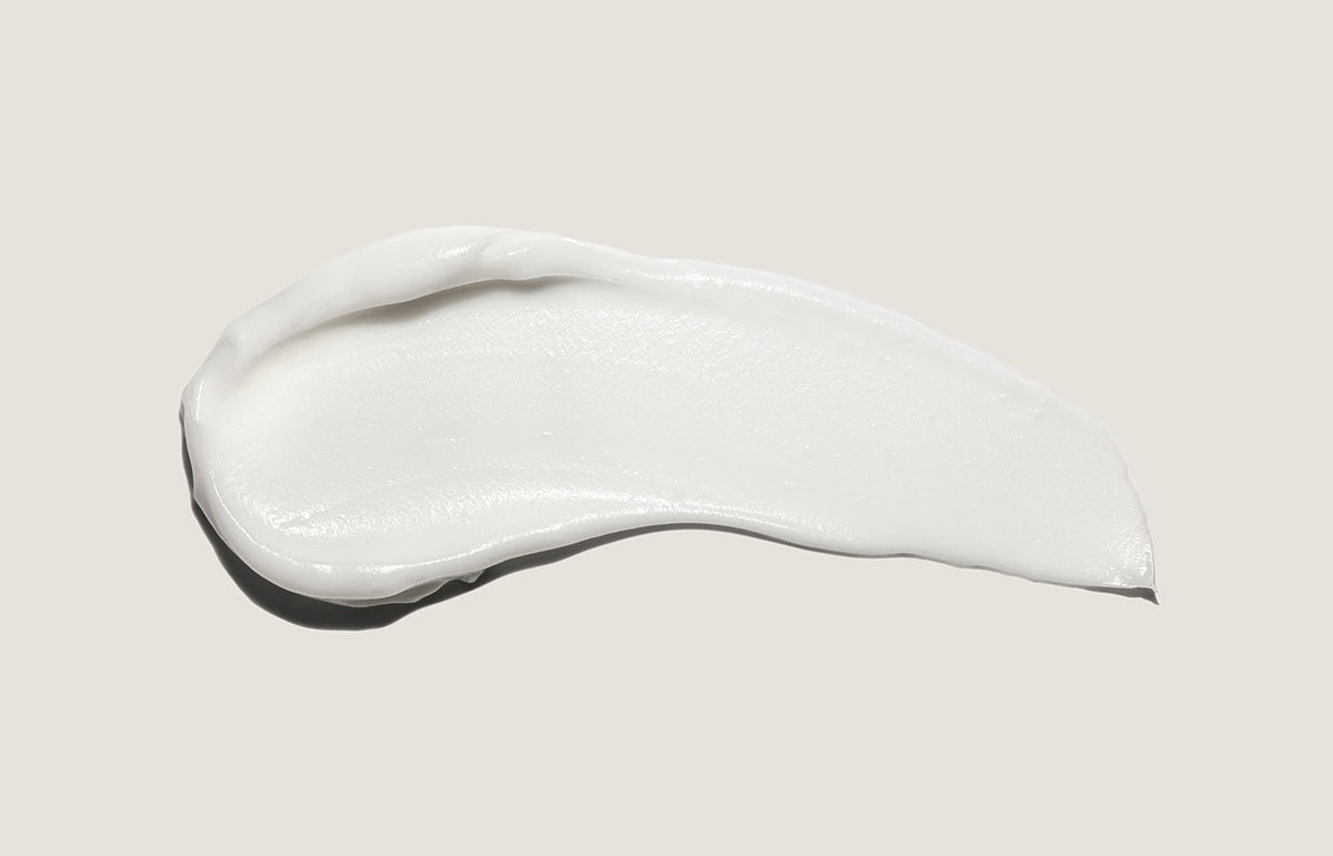 Swatch of white hand cream smeared across a warm grey background