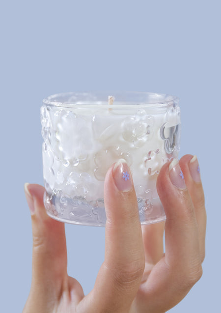 Two hands holding the FLWR Forget Me Not candle against a pale blue backdrop