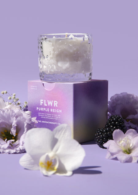 The Purple Reign candle resting on its purple gradient carton, orchids and blackberries below