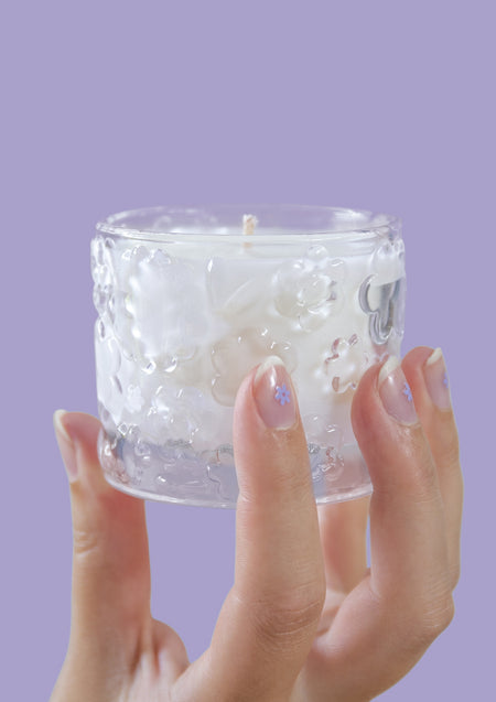 Two hands holding the FLWR Purple Reign candle against a lilac backdrop