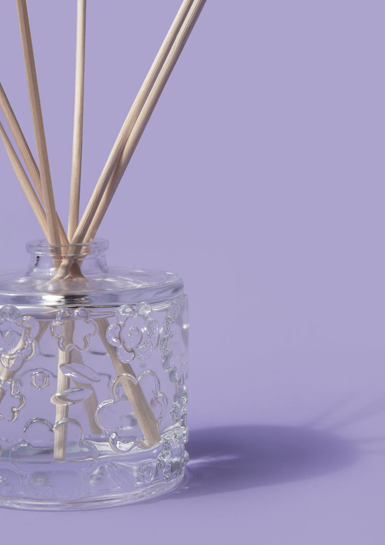 The Purple Reign reed diffuser casting a soft shadow on a plain lilac backdrop