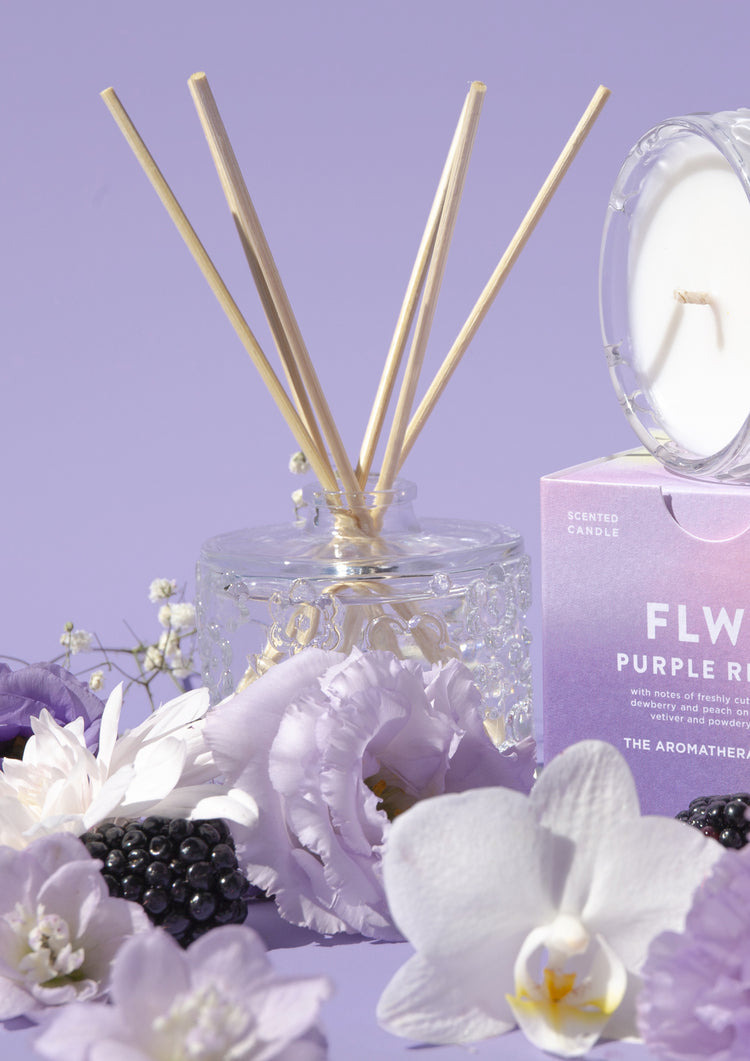 The Purple Reign diffuser with its carton and candle, white orchids and blackberries on lilac