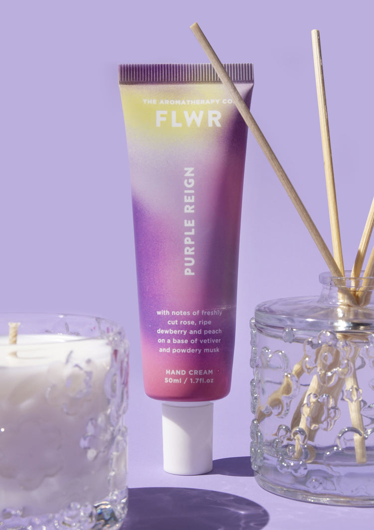 Purple Reign hand cream tube beside a glass candle and reed diffuser on lilac