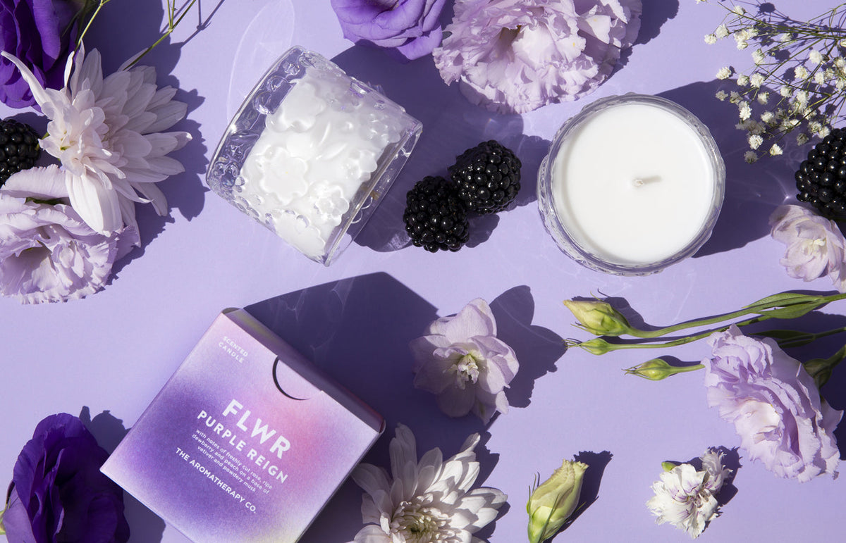 Flat lay of the Purple Reign candle, carton and a second candle among purple blooms and berries