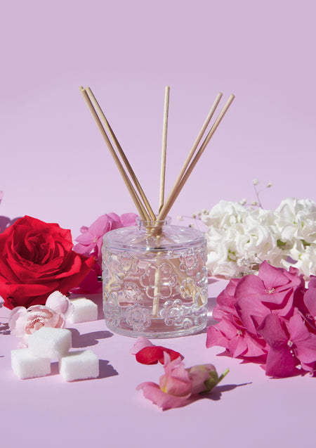 The Sugared Rose diffuser on a lilac backdrop with red and pink roses and sugar cubes