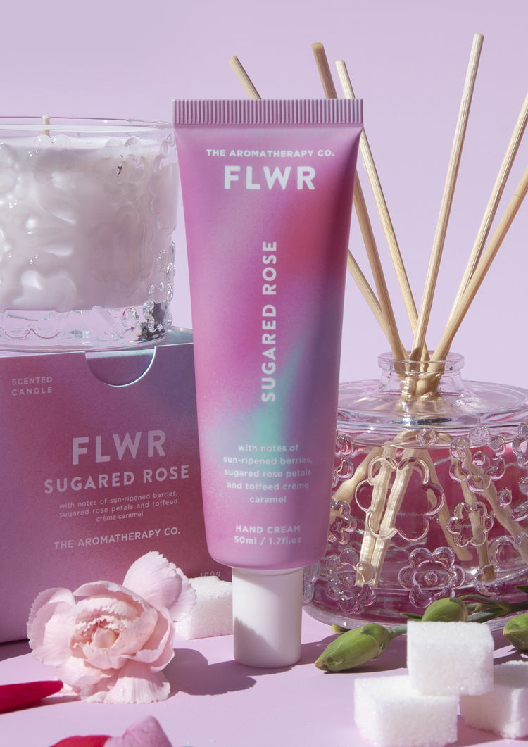 Sugared Rose hand cream tube in front of its box, a glass candle and a reed diffuser